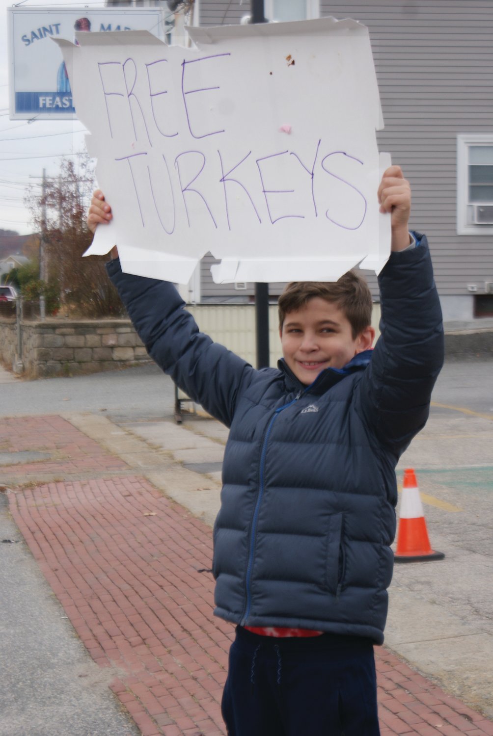 GETTING THE WORD OUT: Holding up a sign at the St. Mary’s Feast Society to draw in more people in need to receive a free frozen turkey is Gunner DeCiccio, age 10.